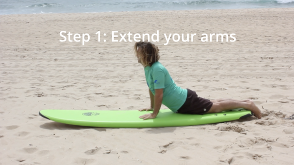 Step 1: Push up and create space.
While laying down on your surfboard, place your hands flat on the board, just beneath your chest, at the bottom of your ribcage, with your fingers pointing toward the rails (sides) of the board. Push up with your arms to lift your chest off the board while angling slightly toward your back foot. This movement creates space between your body and the surfboard, making it easier to place your back foot in the next step.